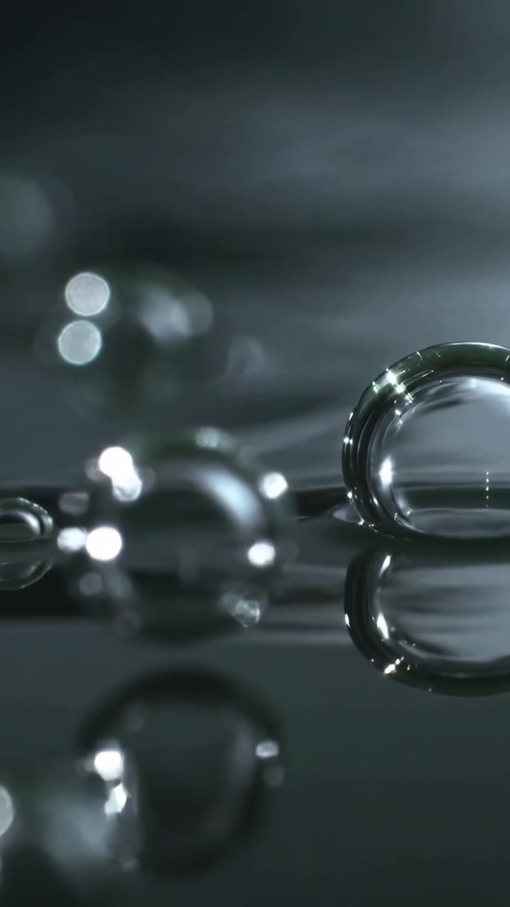 Vertical video: Shifting focus revealing clear bubbles wobbling on dark glossy surface, copy space
