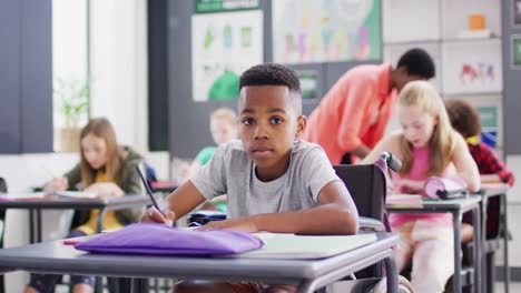 portrait of happy diverse schoolchildren at desks writing in school classroom