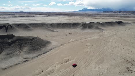 imagen de un avión no tripulado de un vehículo suv rojo moviéndose en un desierto seco y estéril, utah, estados unidos.