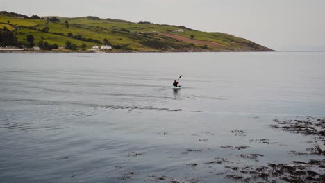 man kayaking in the sea with countryside in background