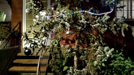 Big-tree-in-front-of-a-house-entrance-decorated-for-Christmas-with-big-ornamental-balls-and-a-strip-of-ornamental-coloured-light-with-different-colour-dots-going-around-it