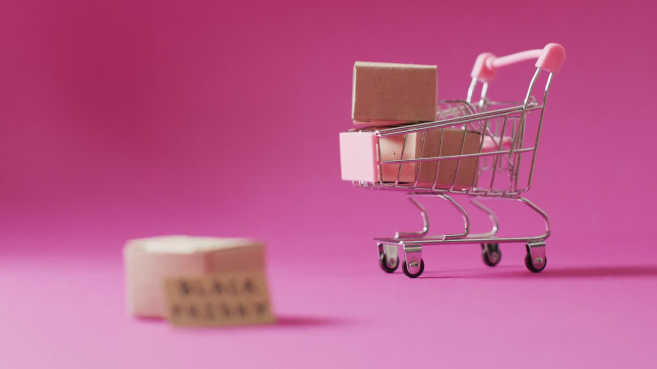 video del texto del viernes negro en cartón y cajas en el carrito de compras sobre fondo rosa