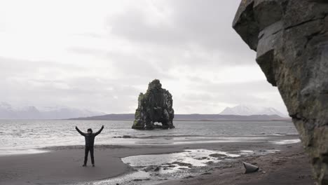 reveal shot of man standing on black sand beach near hvitserkur rock