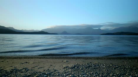 spectacular view of waves gracefully breaking on the serene lake shore, framed by majestic mountains in the background
