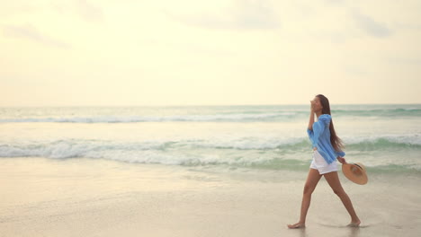 Young-Asian-woman-walks-along-seashore-on-cloudy-day