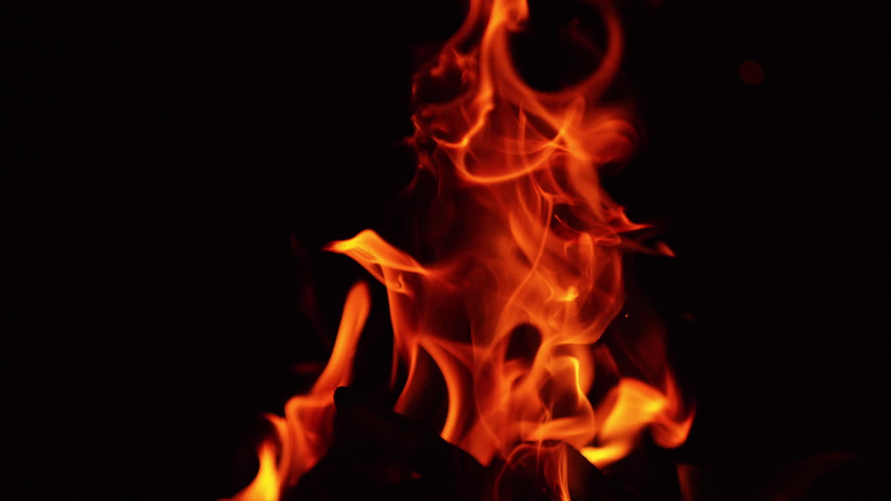 Piled wooden chops burning in the campfire. Fire flames moving to the sides at night. Close up.