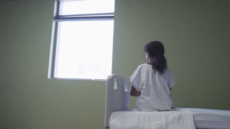 mixed race girl sitting up in hospital bed looking through the window
