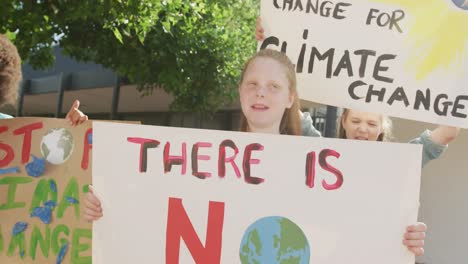 Video-of-diverse-schoolchildren-holding-protest-placards-and-chanting-outdoors,-copy-space