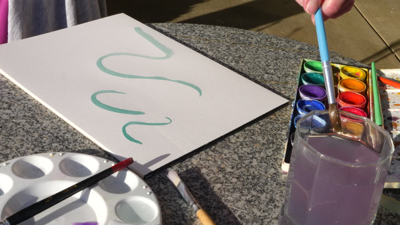 una mujer artista pintando un remolino verde abstracto con acuarela en una mesa en un estudio de arte al aire libre