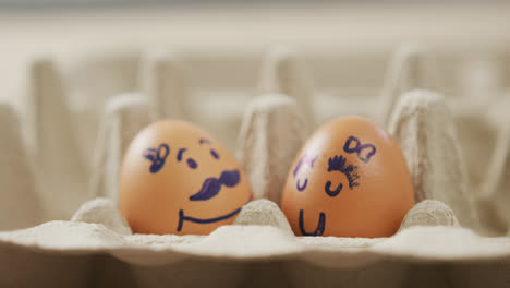 video of close up of two brown eggs with drawn faces in egg carton background