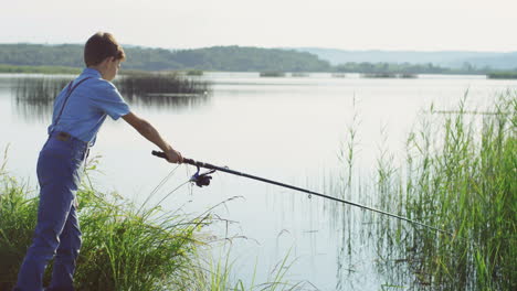 teen boy fishing on the picturesque lake shore with a big rod in the morning on a summer day