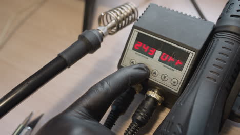 close view of a gloved hand adjusting the digital temperature control on a soldering station, from 234 degrees to 244 degrees and back to 243 degrees