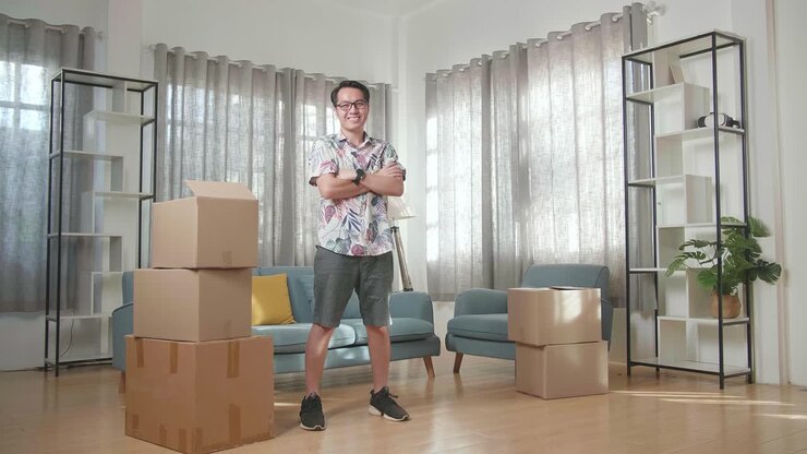 Asian Man With Cardboard Boxes Smiling And Crossing His Arms To Camera In The New House