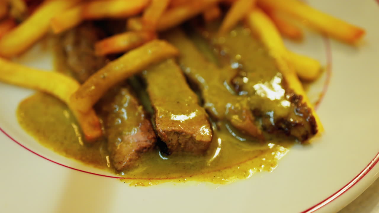 Close up of a plate of fries with meat and green sauce on a plate