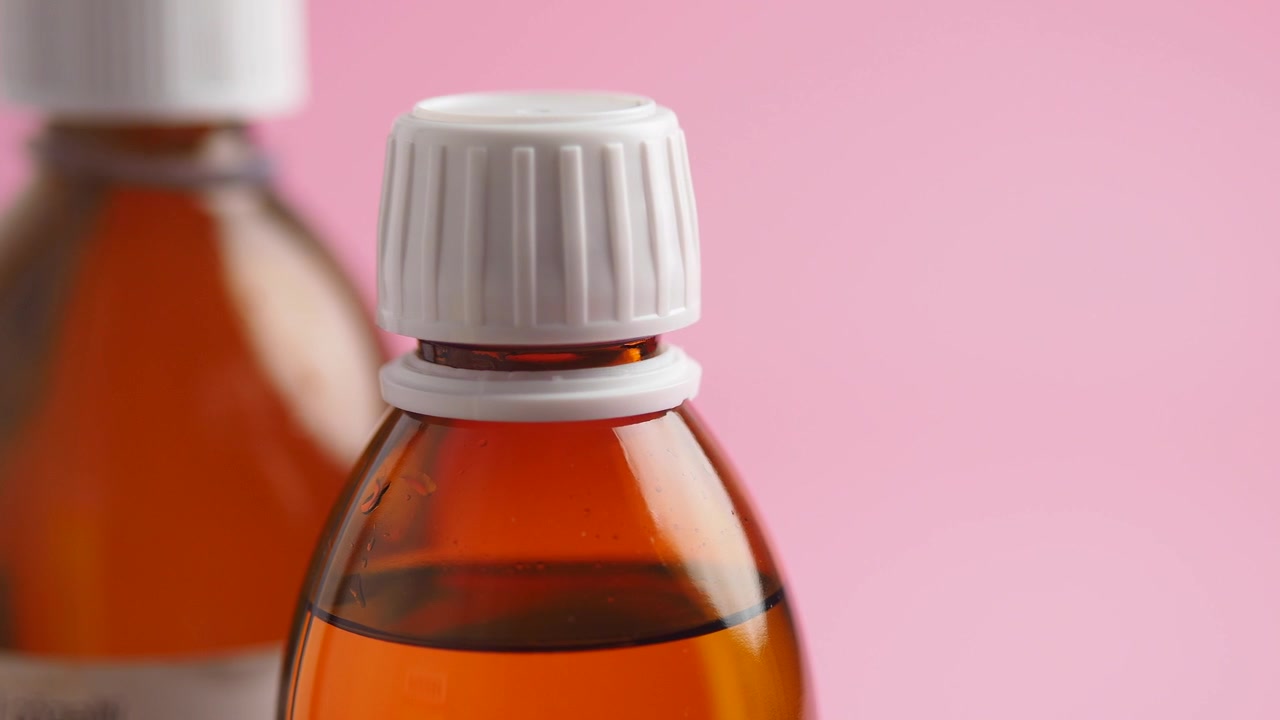 Primer plano de una botella de medicina marrón con tapa blanca sobre fondo rosa