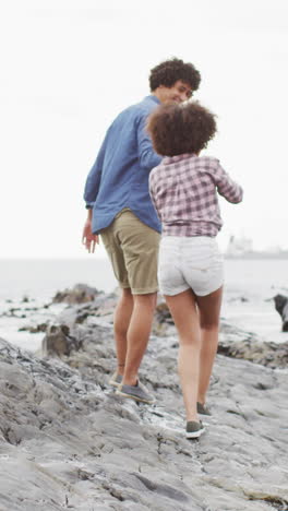 una pareja biracial disfruta de un paseo por la playa rocosa, con espacio para copiar