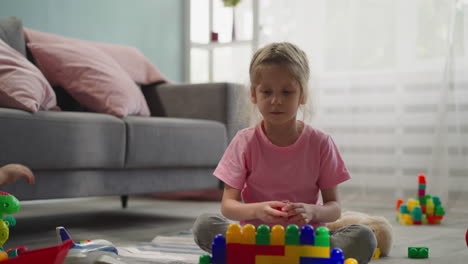 Focused-girl-builds-wall-taking-multi-colored-plastic-blocks