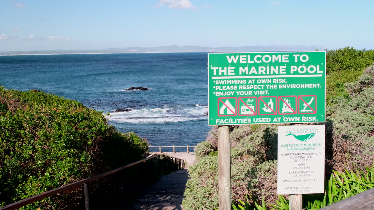 Signage and stairs leading down to scenic marine tide pool in Hermanus. Slider