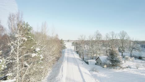 aerial view of a serene winter countryside featuring snow-covered trees, wooden houses, and a winding road through a frosty forest.