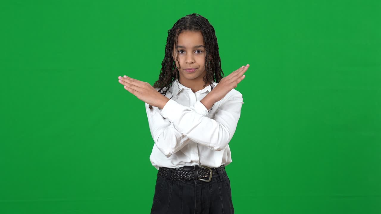 Front view of serious teenage African American girl with crossed hands no gesture posing on green screen shaking head no. Portrait of confident teenager refusing rejecting at chromakey.