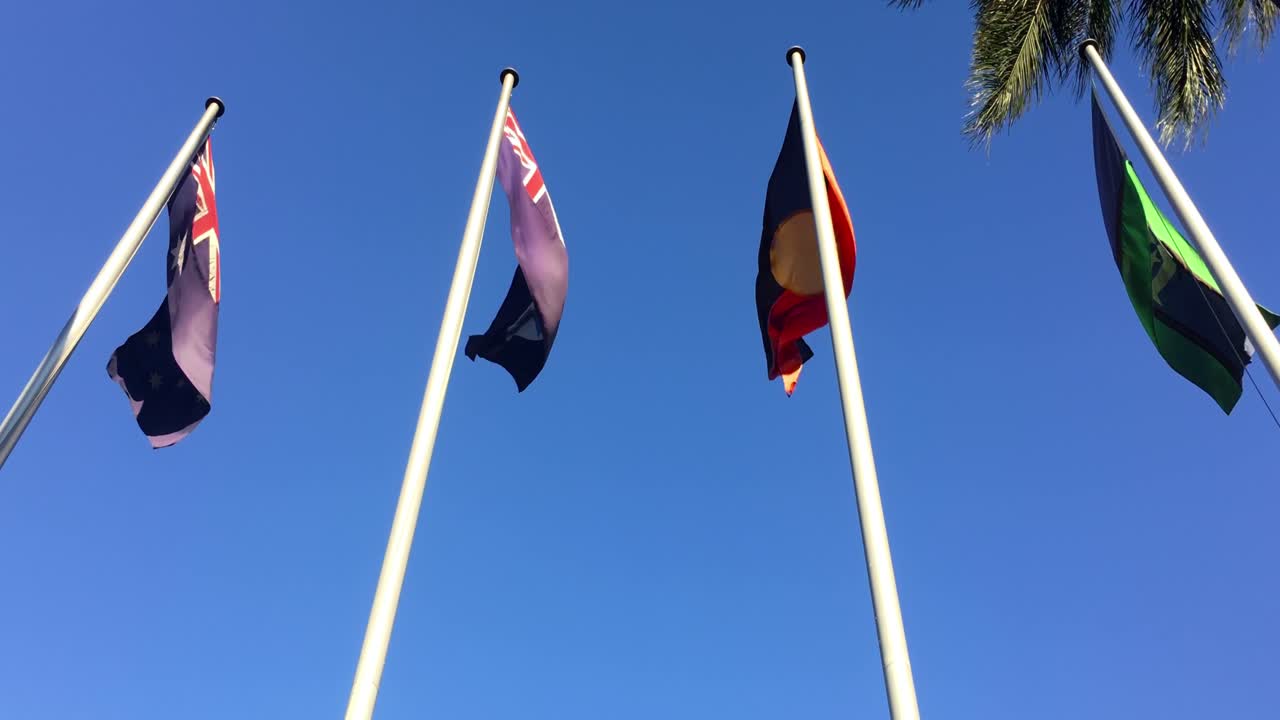 Rich colors of the Australian, Queensland, Aboriginal and Torres Strait Islander flags flying in the wind outside Queensland Parliament House, Brisbane, Australia