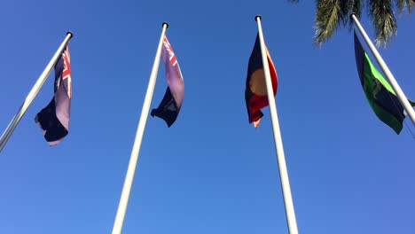 Rich-colors-of-the-Australian,-Queensland,-Aboriginal-and-Torres-Strait-Islander-flags-flying-in-the-wind-outside-Queensland-Parliament-House,-Brisbane,-Australia