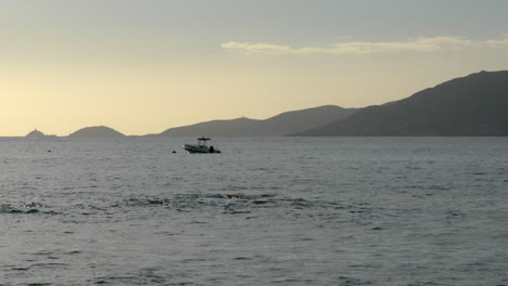escena tranquila del océano, barco anclado, montañas de fondo al atardecer