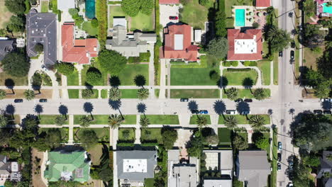 Drone-flies-along-palm-tree-lined-street-with-cars-driving,-and-mansions-in-West-Hollywood,-Los-Angeles,-California