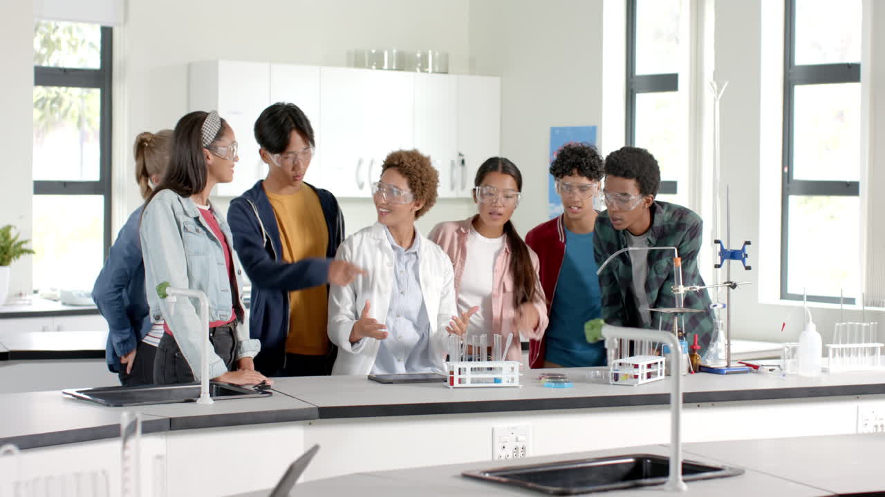 Teenagers in high school laboratory discussing science experiment, wearing safety goggles