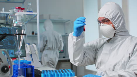scientist in sterile chemistry suit analysing blood sample from test tub