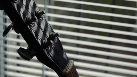 tuning mechanism on a black acoustic guitar by the window