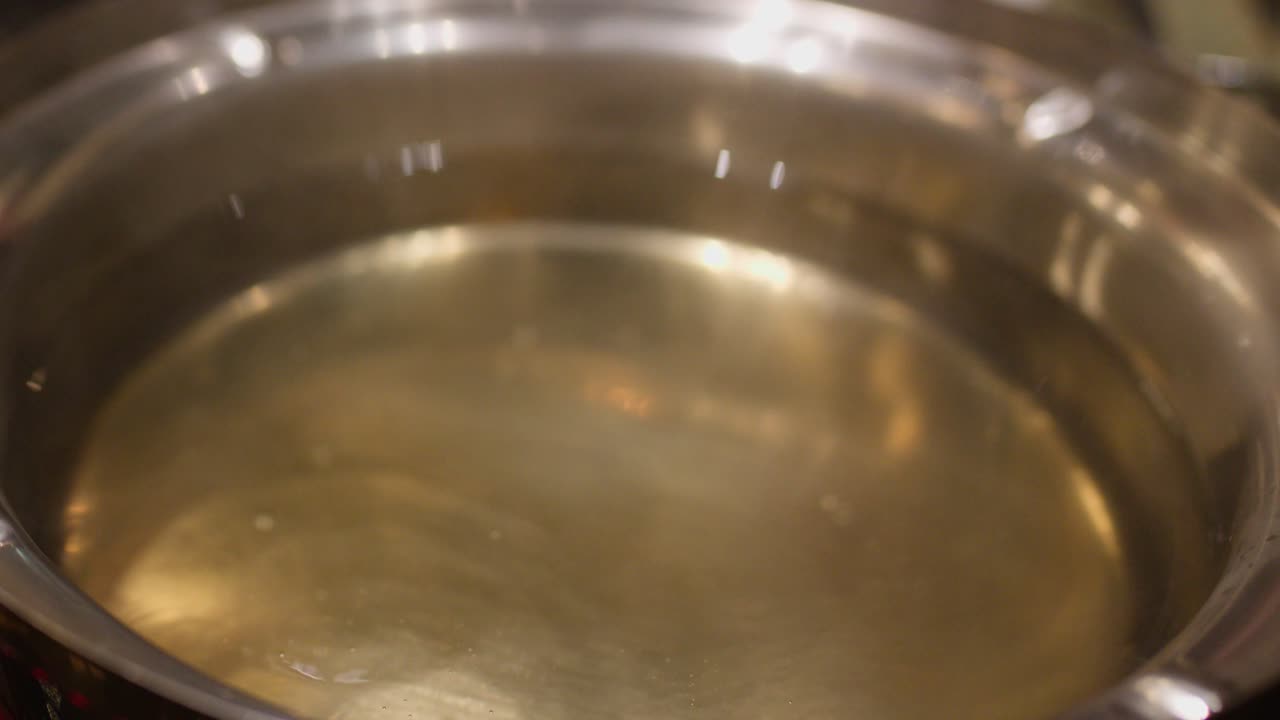 Clear soup broth boils in a metal pot, steam rising gently under soft lighting
