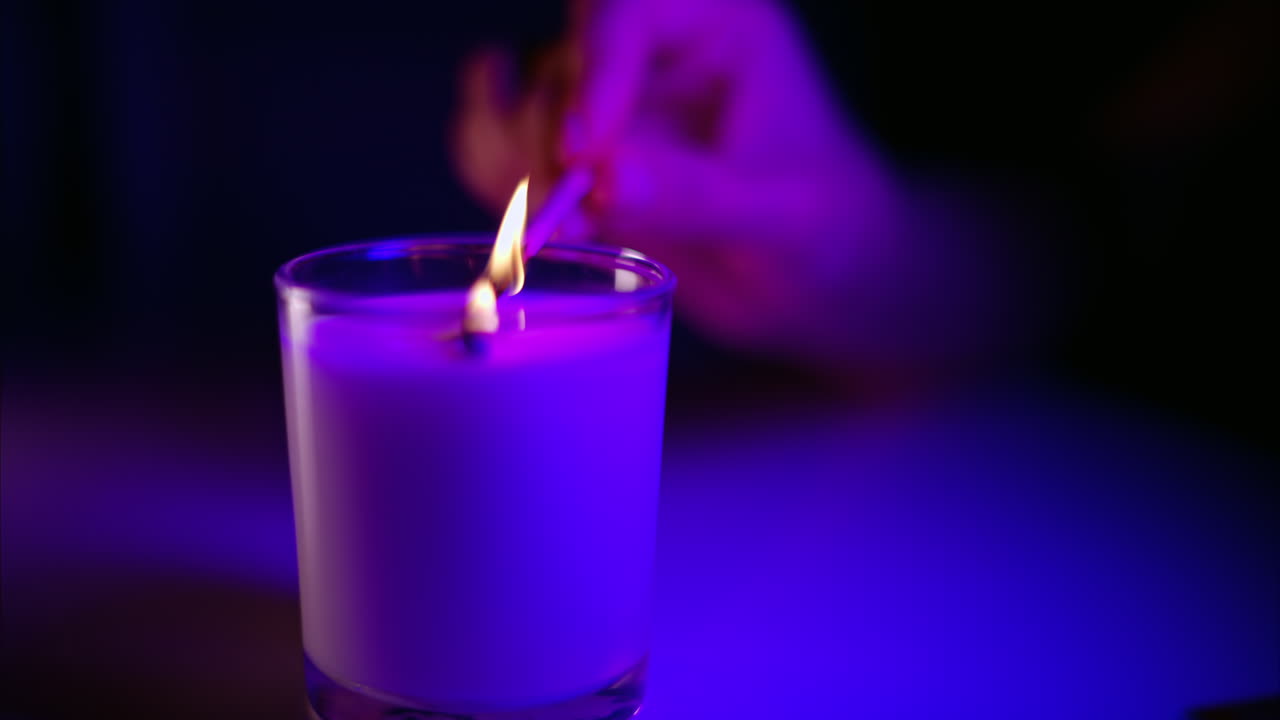 Persona che accende una candela profumata con un fiammifero in un lampo viola