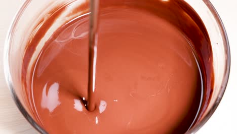 melted chocolate streams into a glass bowl, creating ripples and swirls. warm lighting enhances the rich, glossy texture