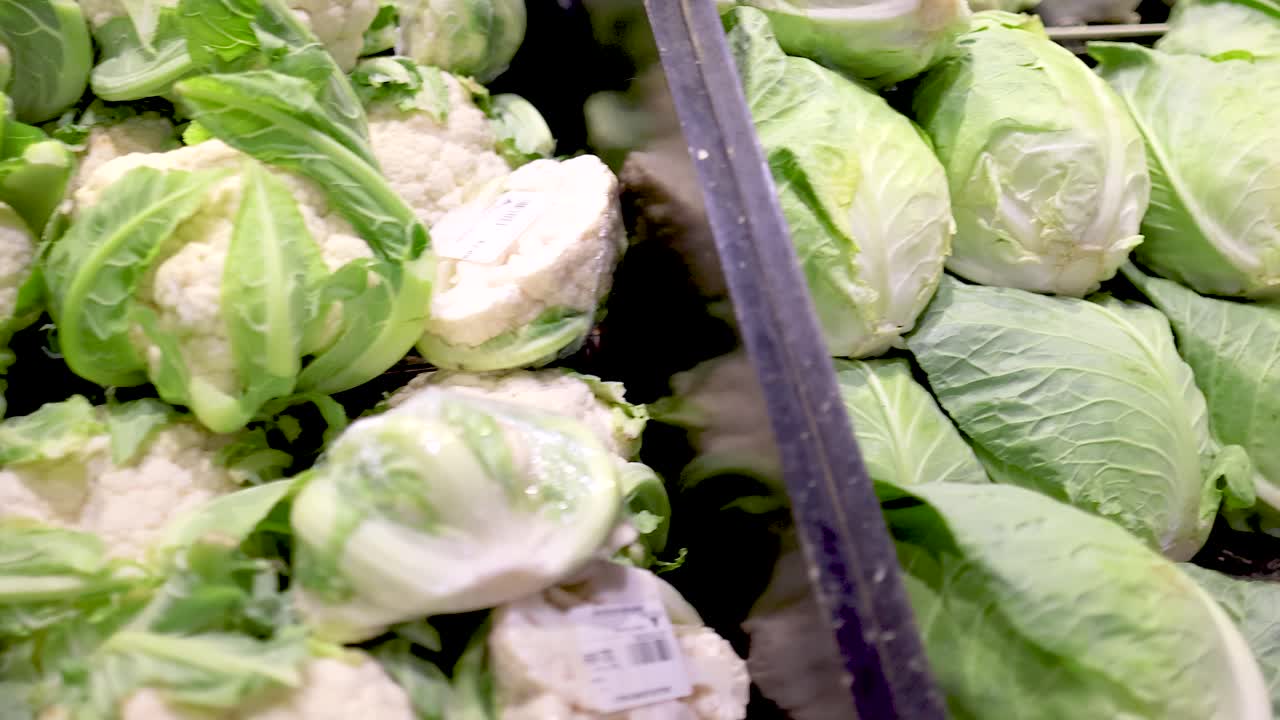 A vibrant display of broccoli, cauliflower, cabbage, and lettuce under bright supermarket lighting