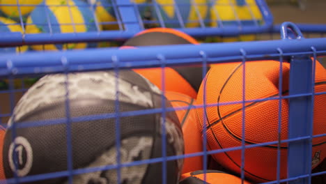 assorted sports balls behind blue mesh cage in a storage room, blurred background