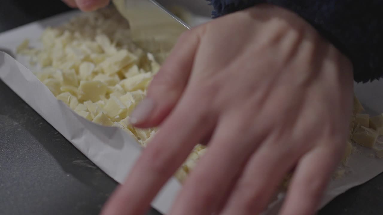 Primo piano: Taglio di una tavoletta di cioccolato bianco a pezzi per la cottura.