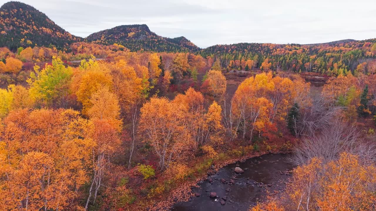 Drone footage shows rushing stream in a rocky gorge with misty hills