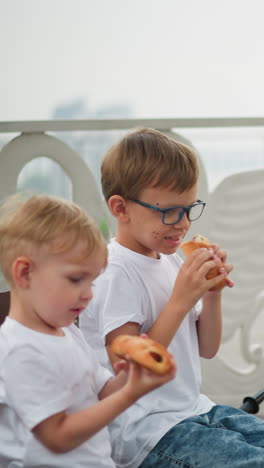 a woman in a blue gown offers a sausage roll to her two children. the older child takes a bite while the younger one watches with curiosity, a black scooter is parked nearby