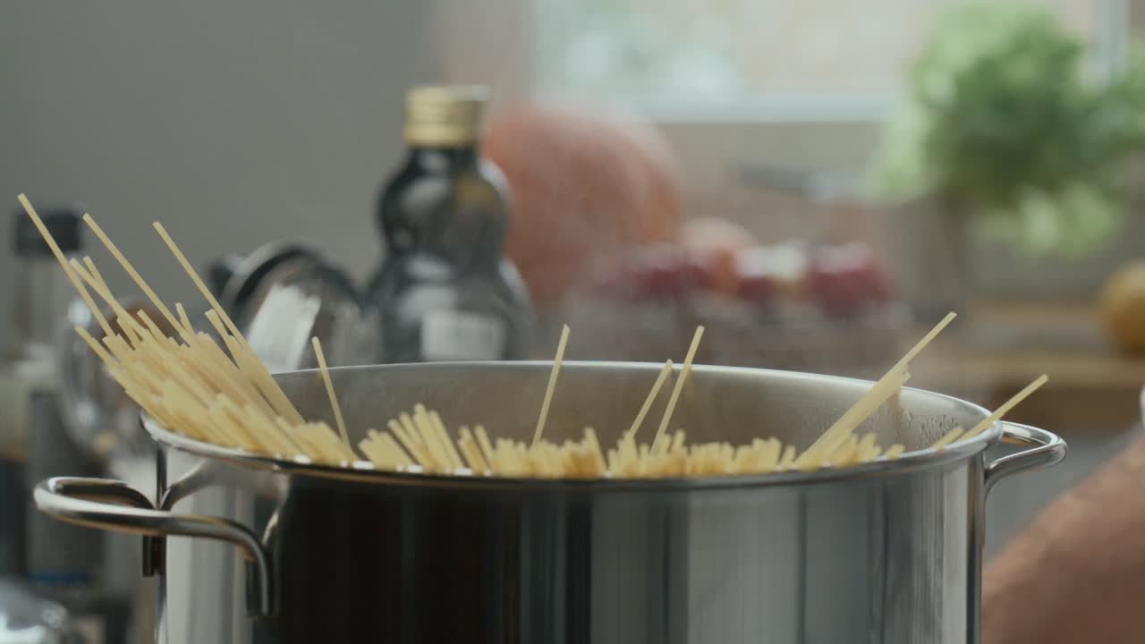Mani che adagiano un mazzo di spaghetti in una pentola di acqua bollente