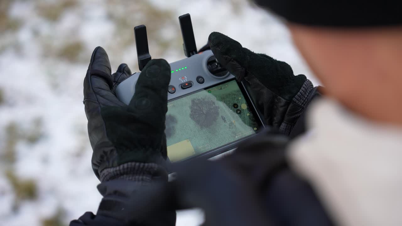 Gloved hands holding drone controller with aerial view display, Czechia