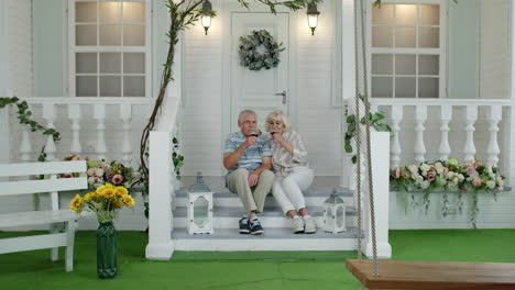 satisfied senior elderly caucasian couple sitting and drinking wine in porch stairs at home