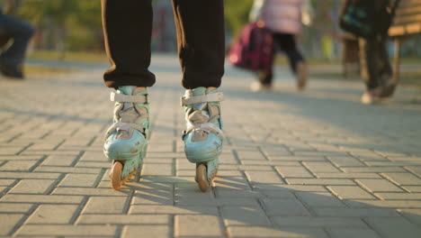 a close-up shot of a person s feet wearing rollerblades, gliding smoothly on a paved path in a park , with other people visible in the blurred background