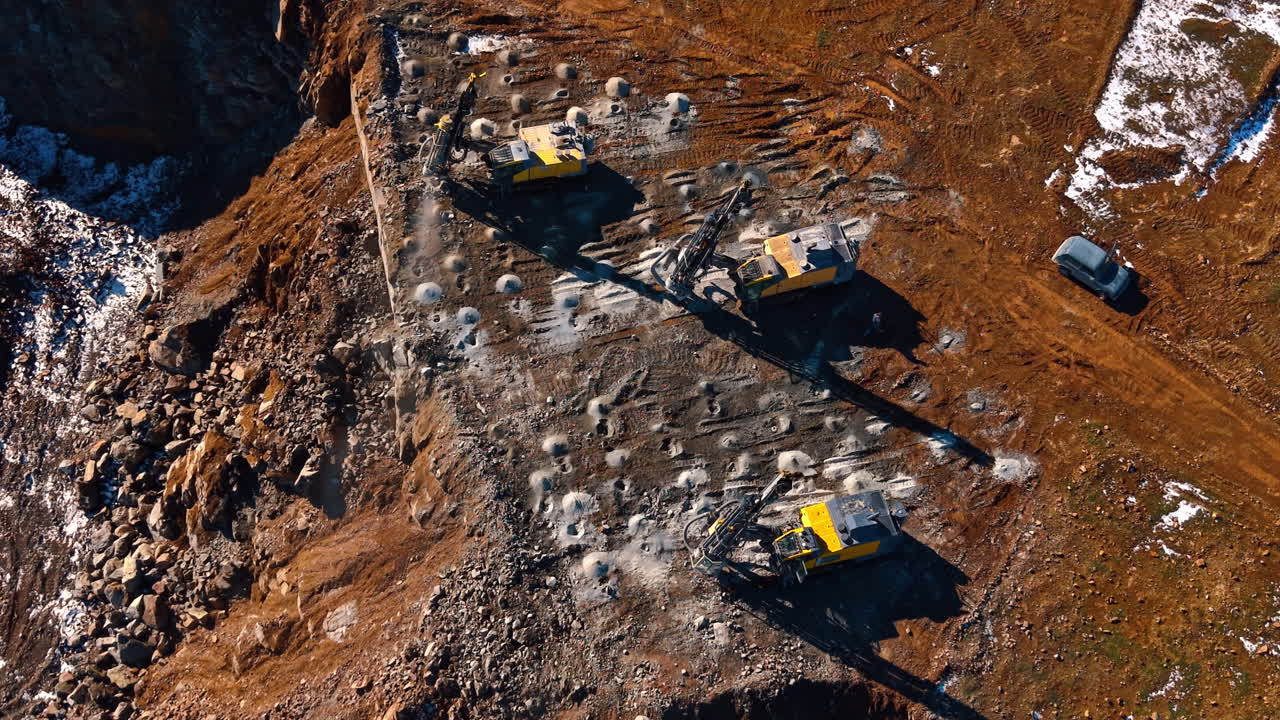 Top down view of three drill rigs in quarry. Symmetrical top view of yellow drilling machines preparing a grid of blast holes on a flat rock bench