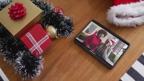 Smiling-african-american-mother-and-daughter-wearing-santa-hats-on-christmas-video-call-on-tablet