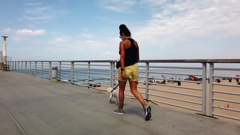 mujer hispana caminando mascota de perro maltés a lo largo del hermoso muelle de playa, california