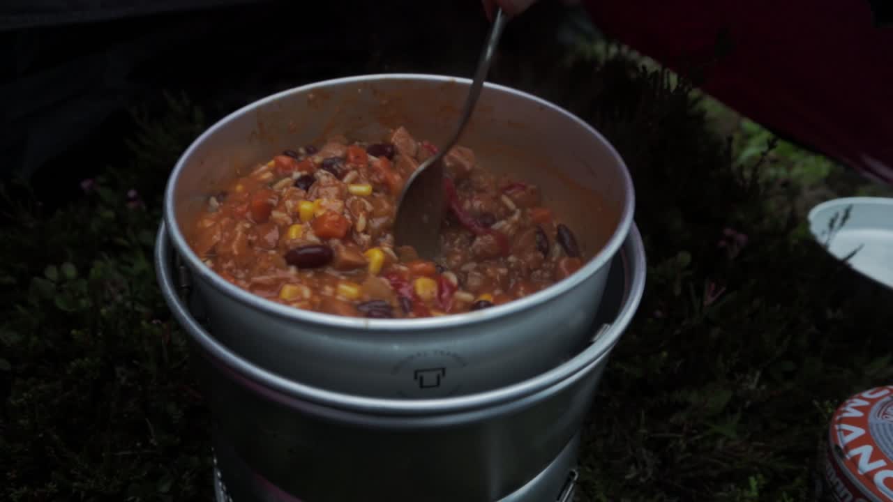 Delicious bean stew being cooked near camping tent, close up move backward view