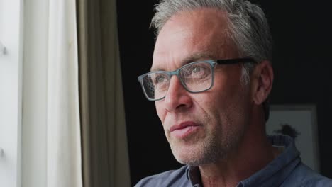 happy caucasian man wearing glasses, looking through window and drinking coffee