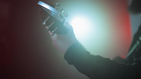 dramatic close-up of a hand strumming a red guitar, highlighted by vibrant colored lighting in a dark room