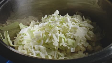 zanahorias picadas que se dejan caer sobre repollo picado, seguidas de arroz seco y sal en un tazón de metal en preparación para el estofado de verduras